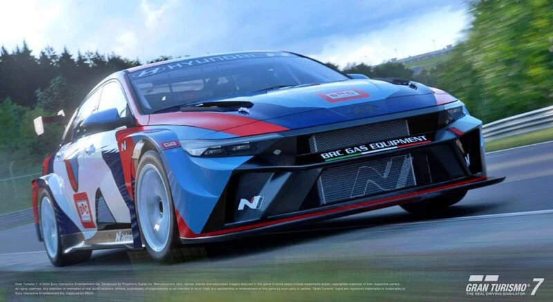 A blue, red, and white Hyundai race car speeds down a track, with trees and a cloudy sky in the background. The