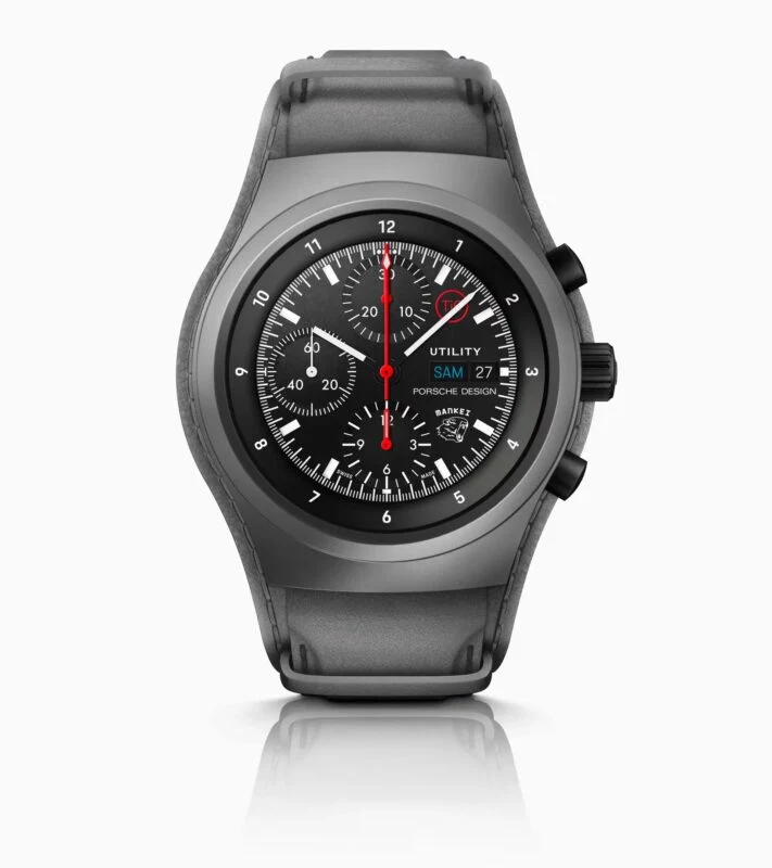 A black Porsche Design chronograph watch with a round face, three subdials, red hands, and a date display is shown against a white background—an ideal addition to any 2025 Holiday Gift Guide.