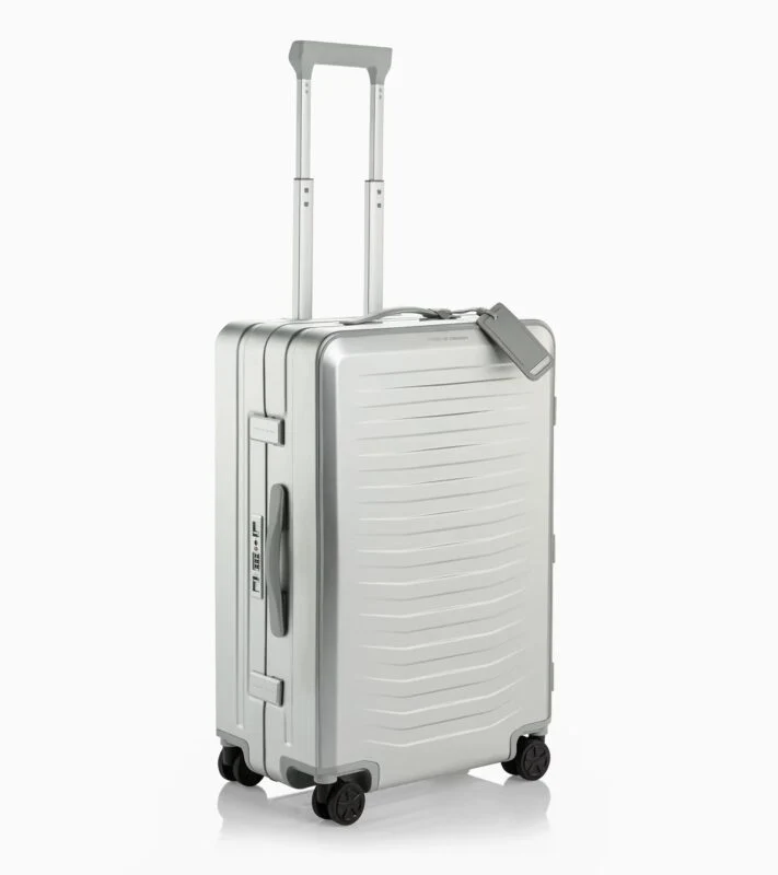 A silver hard-shell suitcase by Porsche Design with four wheels, an extended telescopic handle, side handle, and attached luggage tag stands upright on a white background—an ideal pick for your 2025 Holiday Gift Guide.