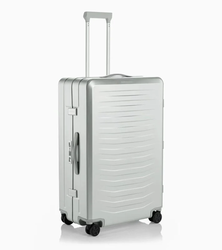 A silver Porsche Design hard-shell rolling suitcase with four wheels, a telescopic handle, and horizontal ridges on the front stands upright on a white background—an elegant choice for any 2025 Holiday Gift Guide.