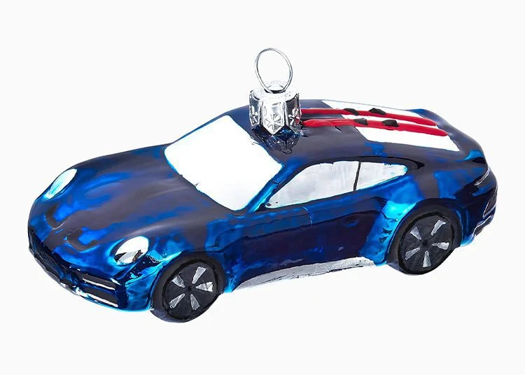 A blue glass car ornament with black wheels, white windows, and red and white racing stripes on the roof—perfect for any Porsche Design fan or as a standout in your 2025 Holiday Gift Guide.