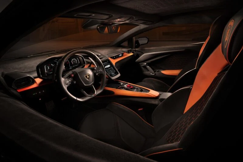 Interior view of the Lamborghini Revuelto luxury sports car featuring black and orange leather seats, a high-tech dashboard with digital displays, and a sleek steering wheel. The cutting-edge specs reflect its premium price, ensuring an unmatched driving experience.