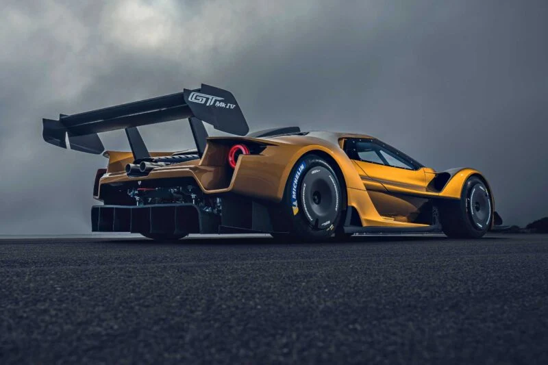 A yellow race car with a large rear wing and slick tires, inspired by the Ford Performance Launches Final Production Run of Legendary Ford GT Mk IV, is parked on an empty asphalt surface under a cloudy sky.