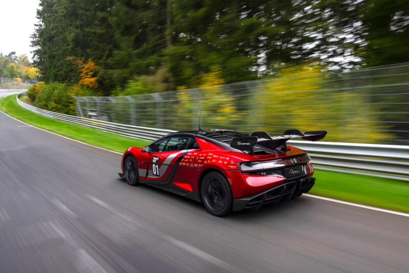 A red YANGWANG U9 electric hypercar with a large rear wing drives on a racetrack surrounded by trees and safety barriers, aiming for a Nürburgring record.
