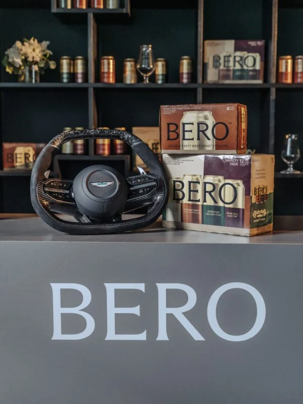A car steering wheel and three boxes of BERO-branded tea are displayed on a counter marked