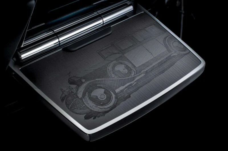 A close-up of a metallic surface engraved with the image of a vintage car, featuring detailed lines and shading, set against a dark background, celebrates Rolls-Royce Honors 100 Years Of Phantom With Groundbreaking Private Collection.