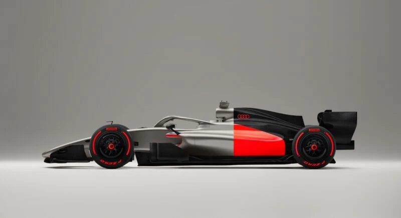 The Audi R26 Concept Formula 1 race car, with a matte silver, black, and red livery and striking red wheel accents, is displayed in a studio setting with a neutral background.
