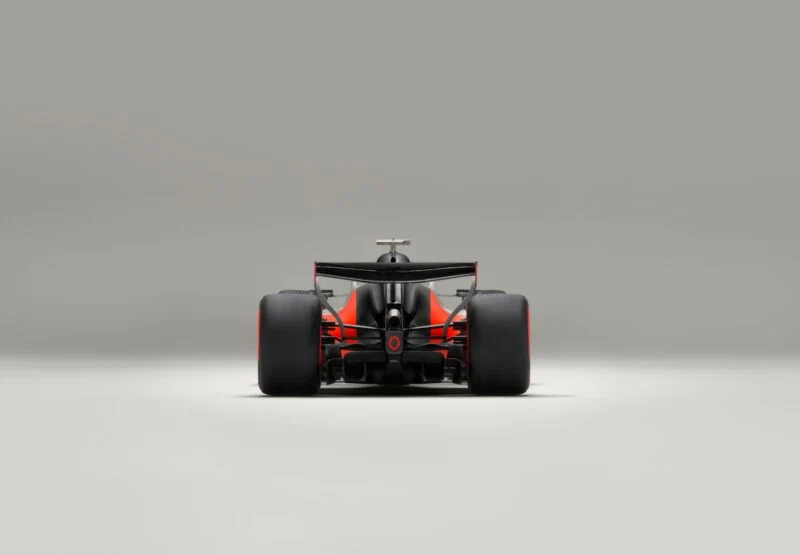 A rear view of a black and orange Audi R26 concept Formula 1 race car on a plain, light gray background.