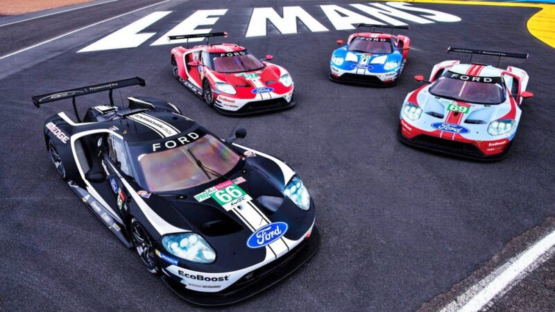 Four Ford GT race cars are parked on the Le Mans racetrack near large white