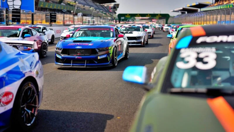 A lineup of colorful race cars, including stunning Ford Le Mans contenders, is parked on the racetrack as drivers prepare for the start of this thrilling motorsport event—echoing excitement for a potential Ford vs Ferrari sequel.