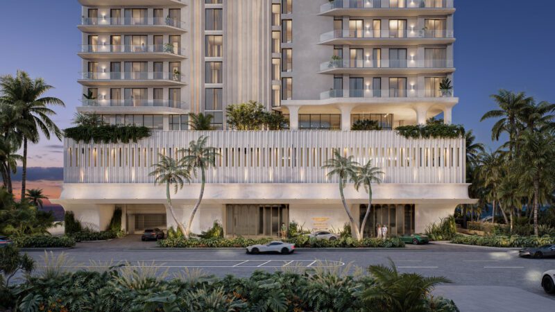 Aston Martin Expands Real Estate Empire With Daytona Beach Shores Residences: A modern high-rise building with balconies and palm trees at the entrance, viewed from the street at dusk, with several cars parked in front.